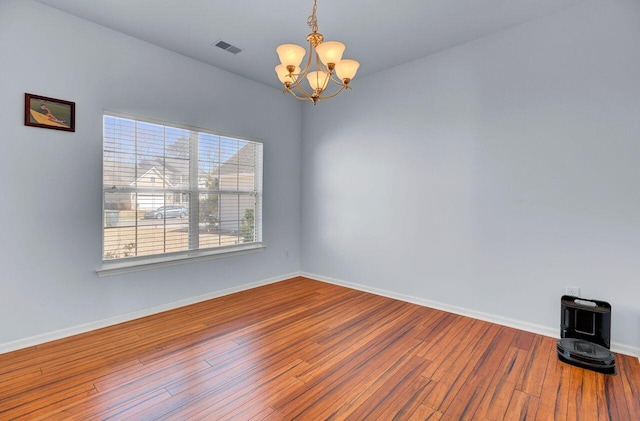 empty room featuring visible vents, wood-type flooring, a notable chandelier, and baseboards