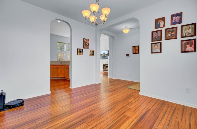 empty room with baseboards, a chandelier, a lit fireplace, hardwood / wood-style floors, and arched walkways