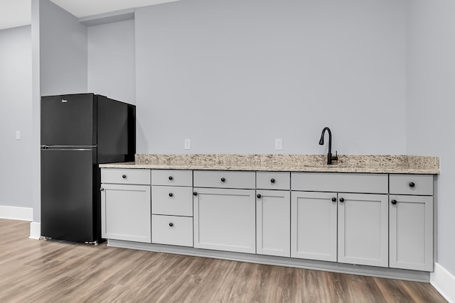 kitchen with a sink, light stone counters, light wood-style floors, and freestanding refrigerator