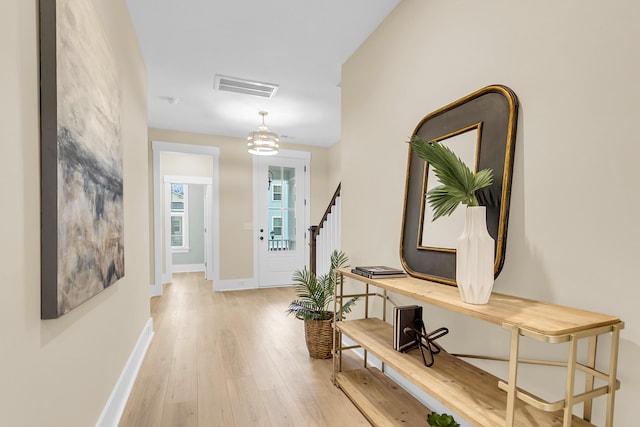 corridor featuring stairs, light wood-style floors, visible vents, and baseboards