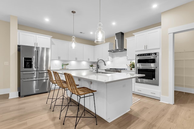 kitchen with a sink, light countertops, a kitchen breakfast bar, appliances with stainless steel finishes, and wall chimney range hood