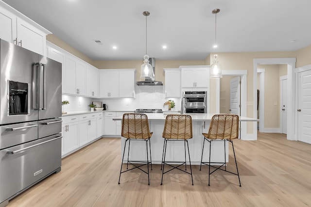 kitchen featuring wall chimney range hood, light countertops, decorative backsplash, appliances with stainless steel finishes, and white cabinets