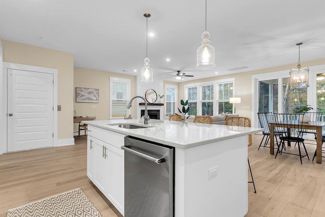 kitchen with stainless steel dishwasher, light wood-style flooring, a fireplace, and a sink