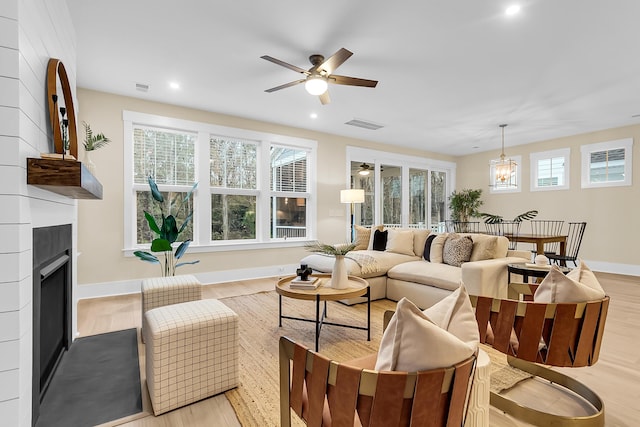 living area featuring light wood-style flooring, ceiling fan with notable chandelier, visible vents, and a large fireplace