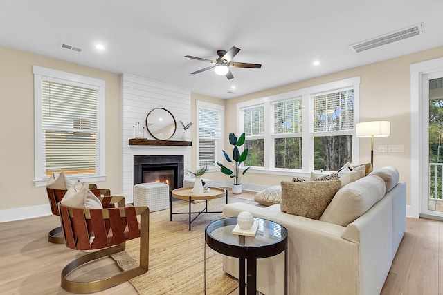 living room with light wood-type flooring, visible vents, ceiling fan, and a fireplace