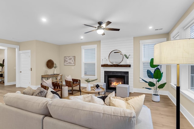 living area featuring visible vents, a large fireplace, baseboards, ceiling fan, and wood finished floors