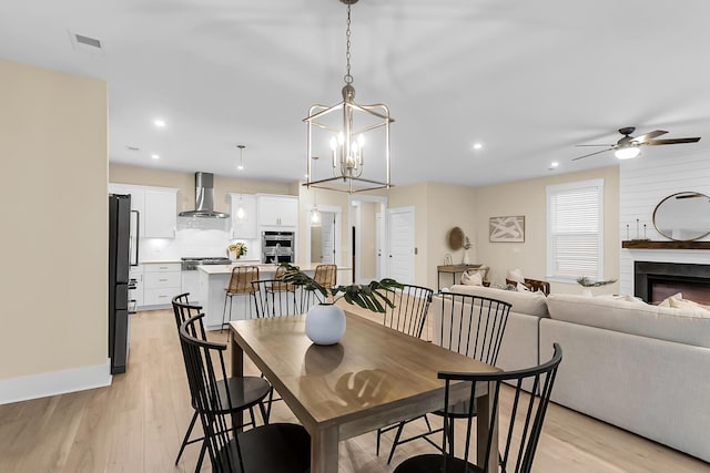 dining area featuring visible vents, ceiling fan with notable chandelier, recessed lighting, a large fireplace, and light wood finished floors