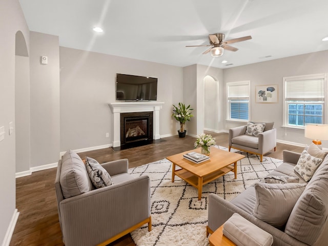 living area featuring a ceiling fan, wood finished floors, arched walkways, and baseboards