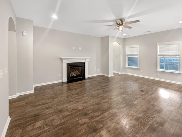 unfurnished living room featuring arched walkways, baseboards, dark wood-type flooring, and a ceiling fan