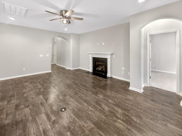 unfurnished living room with visible vents, a fireplace with flush hearth, dark wood-type flooring, arched walkways, and ceiling fan