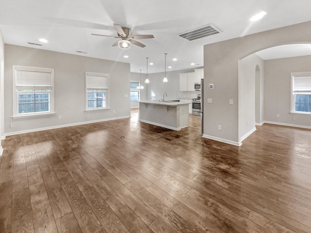 unfurnished living room with visible vents, a ceiling fan, a sink, dark wood finished floors, and arched walkways