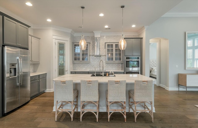 kitchen featuring appliances with stainless steel finishes, gray cabinetry, a center island with sink, and wall chimney exhaust hood