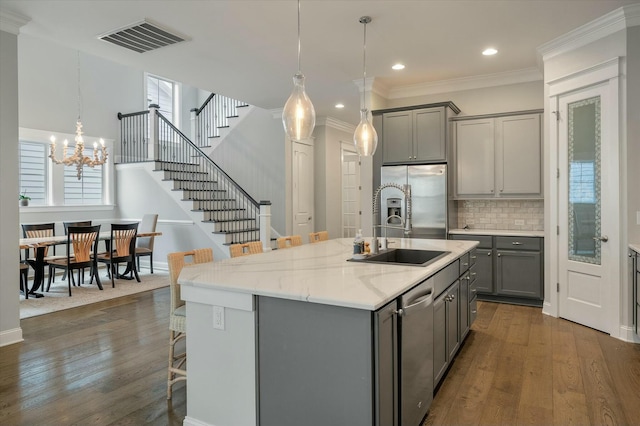 kitchen with sink, a breakfast bar area, a center island with sink, gray cabinets, and stainless steel appliances