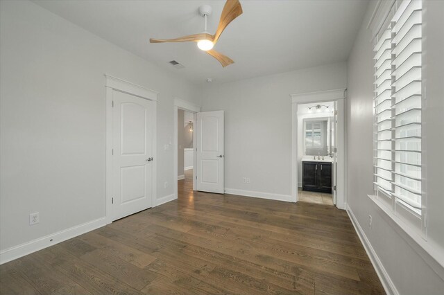 unfurnished bedroom with ensuite bathroom, dark wood-type flooring, and ceiling fan