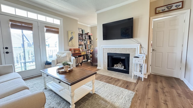 living area with baseboards, a tile fireplace, ornamental molding, wood finished floors, and a textured ceiling