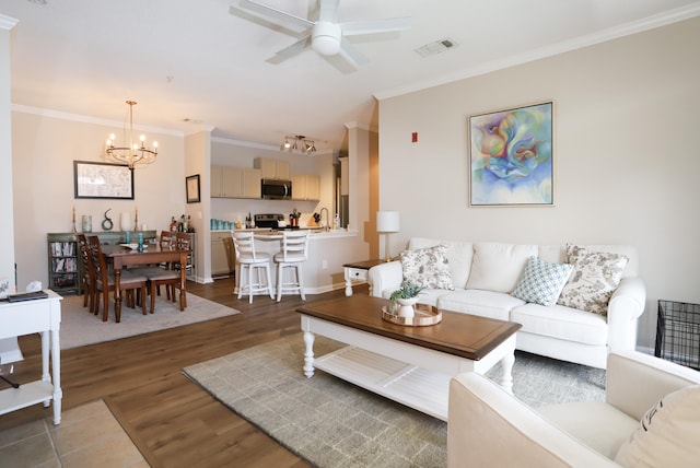 living area with ceiling fan with notable chandelier, wood finished floors, visible vents, baseboards, and ornamental molding