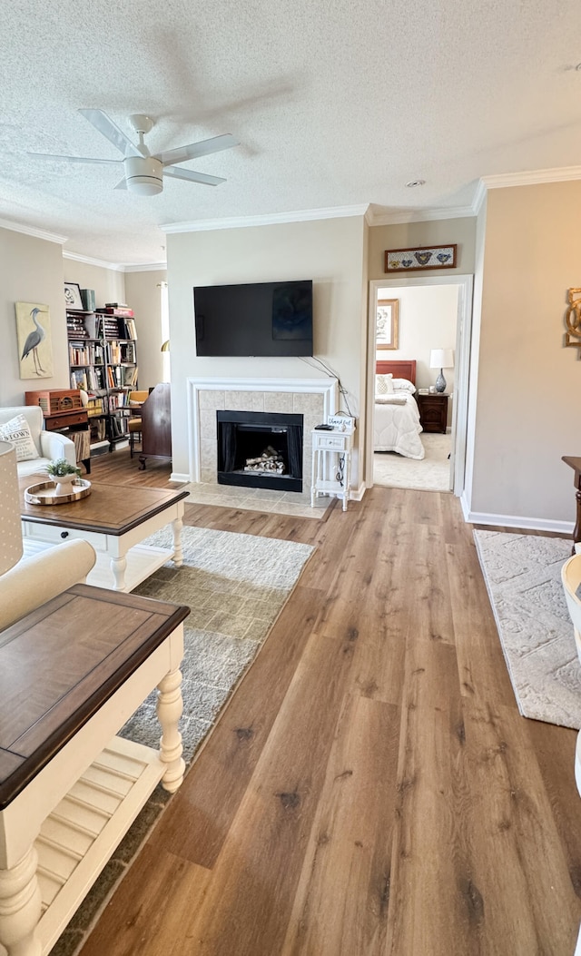 living room with a textured ceiling, a fireplace, crown molding, and wood finished floors