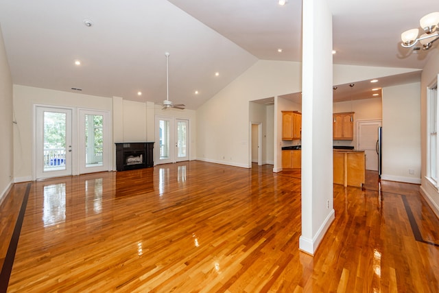 unfurnished living room with ceiling fan with notable chandelier, light hardwood / wood-style floors, and high vaulted ceiling