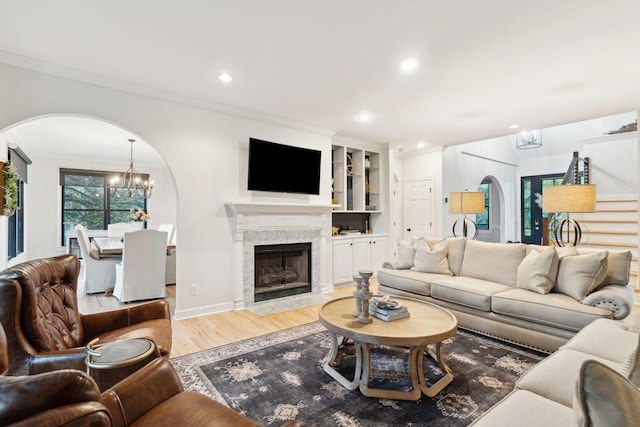 living room with crown molding, a fireplace, a chandelier, and light hardwood / wood-style floors