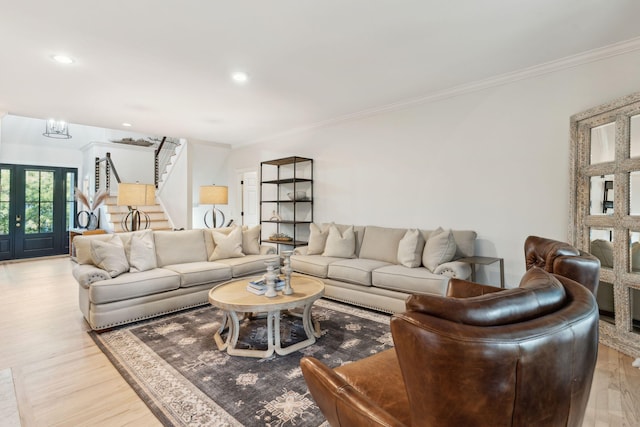 living room with crown molding, an inviting chandelier, light hardwood / wood-style floors, and french doors