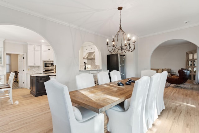 dining area featuring sink, a notable chandelier, ornamental molding, and light hardwood / wood-style floors