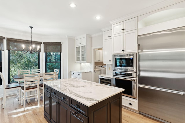 kitchen featuring separate washer and dryer, white cabinets, built in appliances, crown molding, and light wood-type flooring