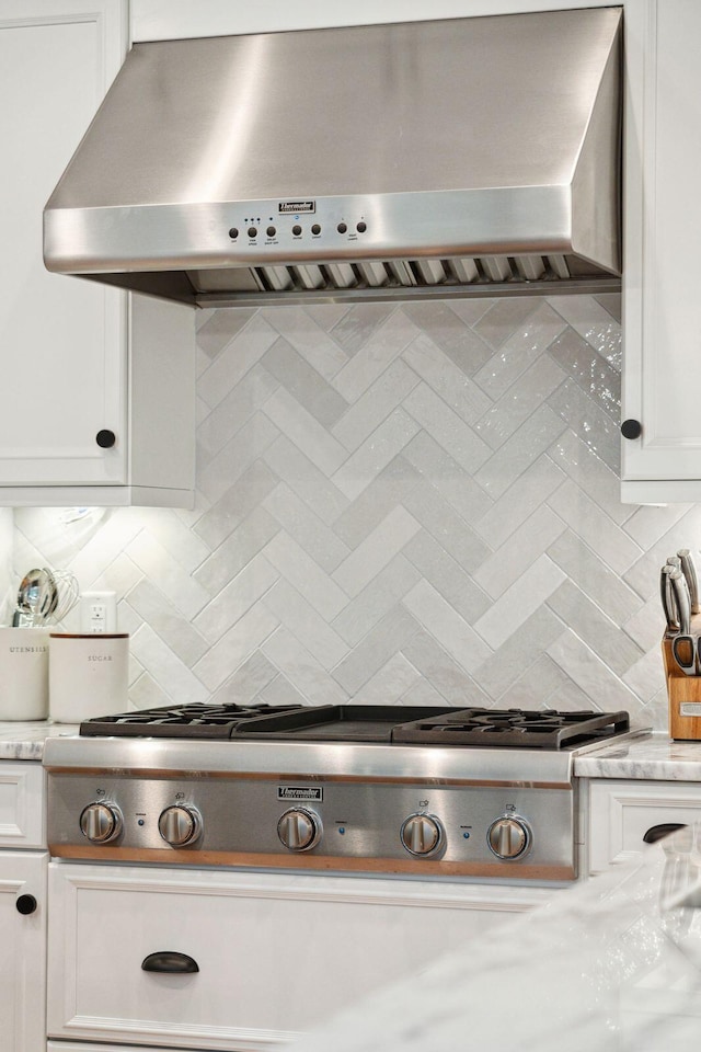 details featuring wall chimney exhaust hood, stainless steel gas cooktop, tasteful backsplash, light stone countertops, and white cabinets