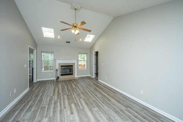 unfurnished living room with a skylight, ceiling fan, light hardwood / wood-style flooring, high vaulted ceiling, and a tiled fireplace