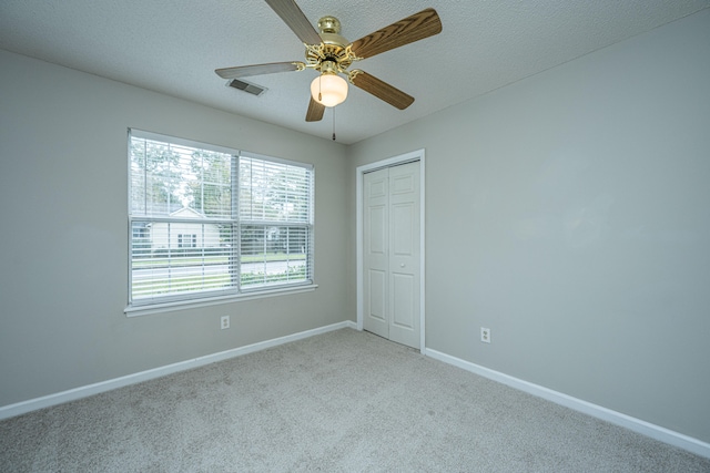 unfurnished bedroom with light carpet, a textured ceiling, a closet, and ceiling fan