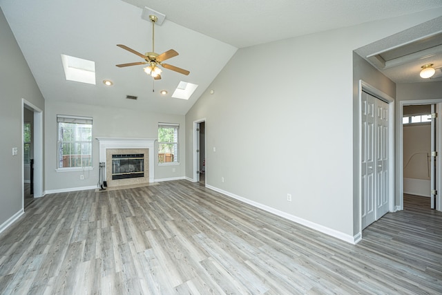 unfurnished living room with a skylight, ceiling fan, light hardwood / wood-style flooring, high vaulted ceiling, and a tiled fireplace