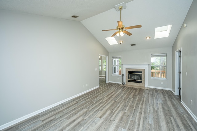 unfurnished living room featuring vaulted ceiling with skylight, ceiling fan, light wood-type flooring, and a textured ceiling