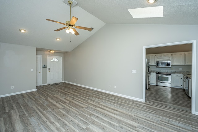 unfurnished living room featuring light wood-type flooring, a skylight, high vaulted ceiling, and ceiling fan