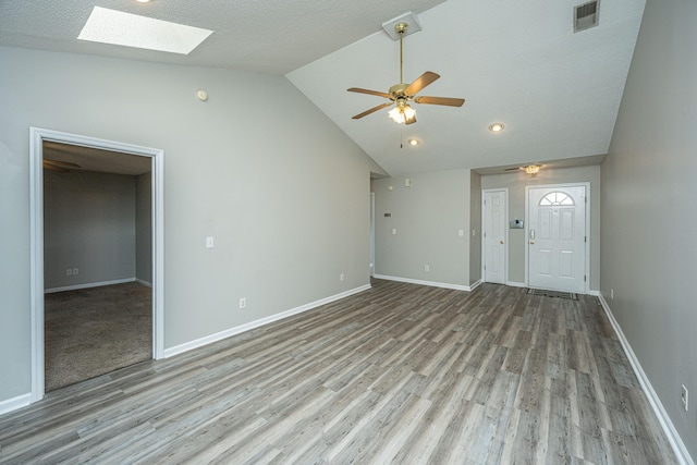 unfurnished living room featuring ceiling fan, vaulted ceiling with skylight, a textured ceiling, and light wood-type flooring