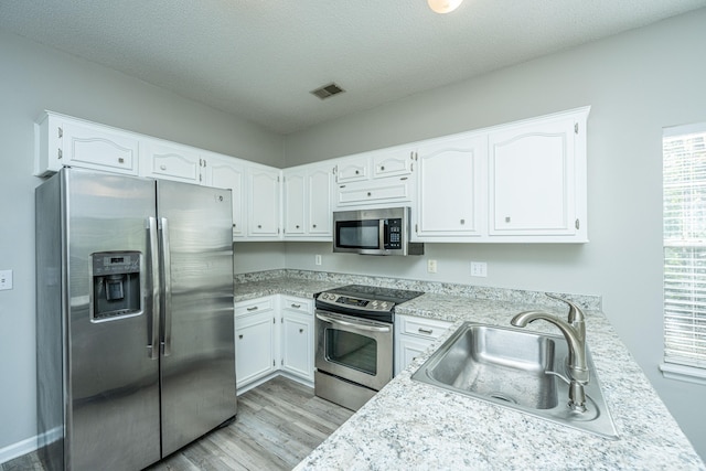 kitchen featuring sink, a textured ceiling, light hardwood / wood-style floors, white cabinetry, and stainless steel appliances