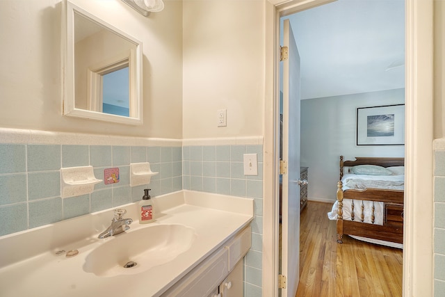 bathroom featuring a wainscoted wall, tile walls, connected bathroom, vanity, and wood finished floors