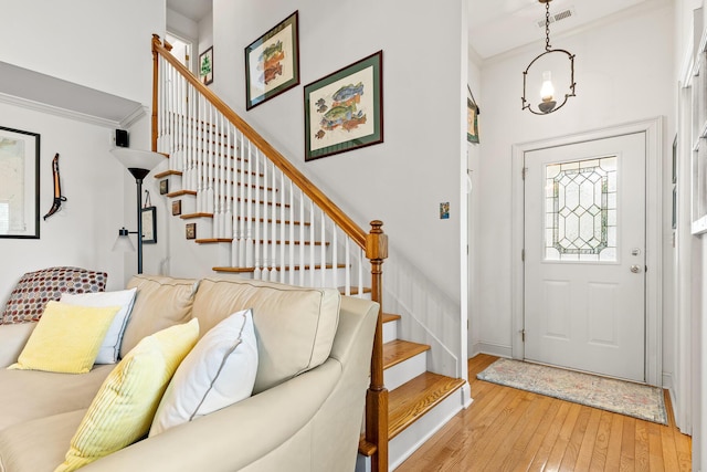 entryway with visible vents, ornamental molding, stairway, and light wood-type flooring