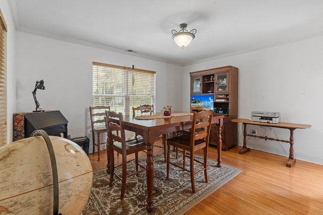 dining area featuring light wood-style floors, baseboards, ornamental molding, and visible vents