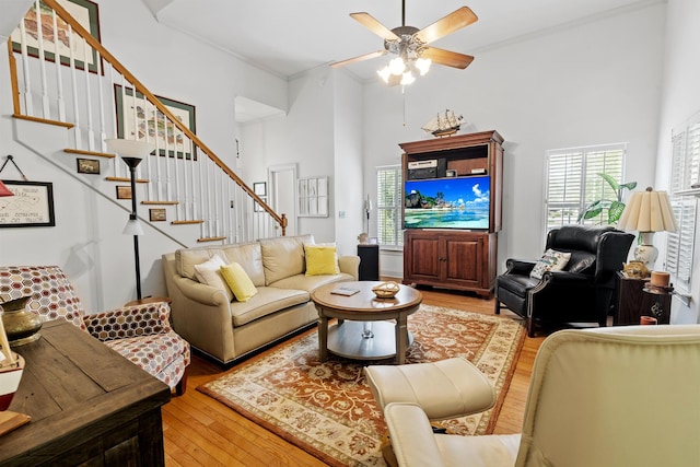 living area with light wood-style floors, a towering ceiling, stairway, and ceiling fan