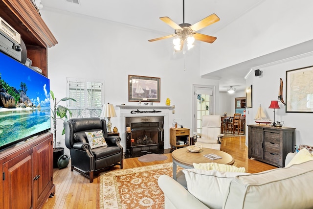 living room featuring light wood finished floors, a ceiling fan, a high end fireplace, a towering ceiling, and visible vents