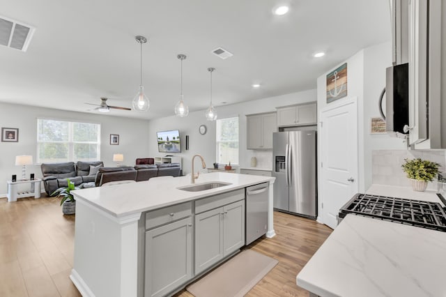 kitchen with a center island with sink, appliances with stainless steel finishes, light stone countertops, ceiling fan, and sink