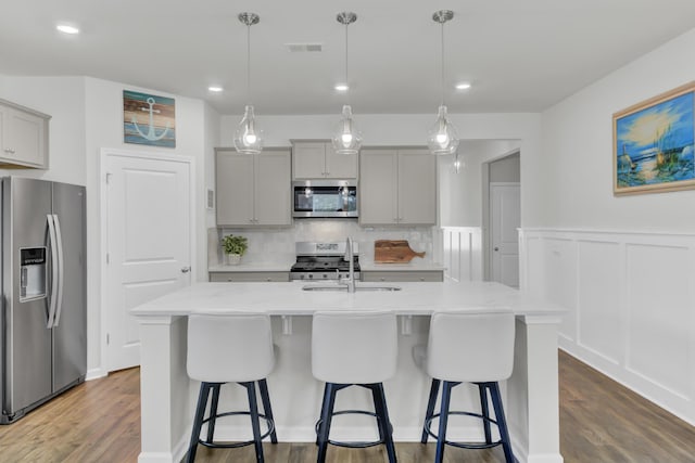 kitchen with a center island with sink, appliances with stainless steel finishes, gray cabinets, and hanging light fixtures