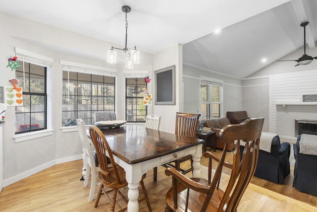 dining space featuring light wood-style flooring, baseboards, a brick fireplace, ceiling fan, and vaulted ceiling