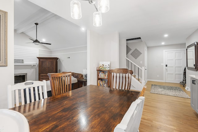 dining space featuring vaulted ceiling with beams, stairs, light wood-style flooring, a fireplace, and a ceiling fan