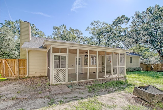 back of property with a gate, a chimney, fence, and a sunroom