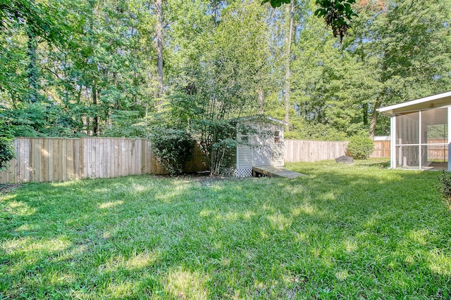 view of yard featuring a fenced backyard, a storage unit, an outdoor structure, and a sunroom