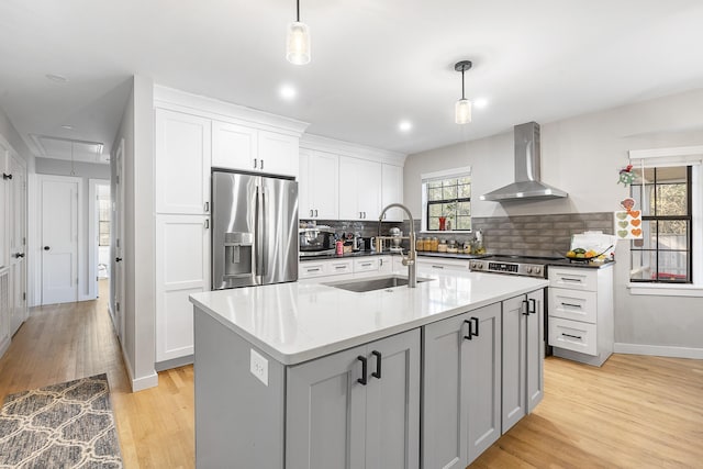 kitchen featuring wall chimney range hood, light wood-style flooring, hanging light fixtures, stainless steel fridge, and a sink