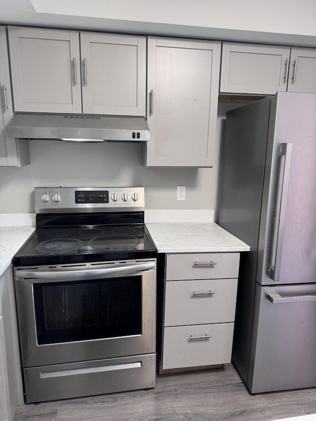 kitchen with light stone countertops, hardwood / wood-style floors, stainless steel appliances, and gray cabinetry