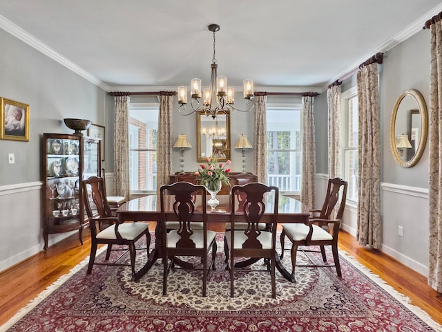 dining area with wood-type flooring, a wealth of natural light, crown molding, and a chandelier