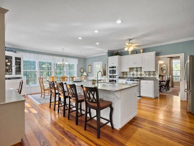 kitchen with white cabinets, stainless steel appliances, decorative backsplash, hanging light fixtures, and a large island