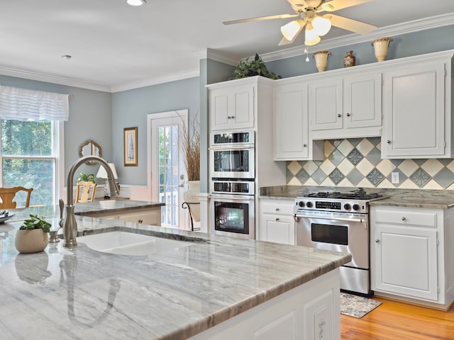 kitchen with backsplash, sink, white cabinetry, stainless steel appliances, and light stone counters